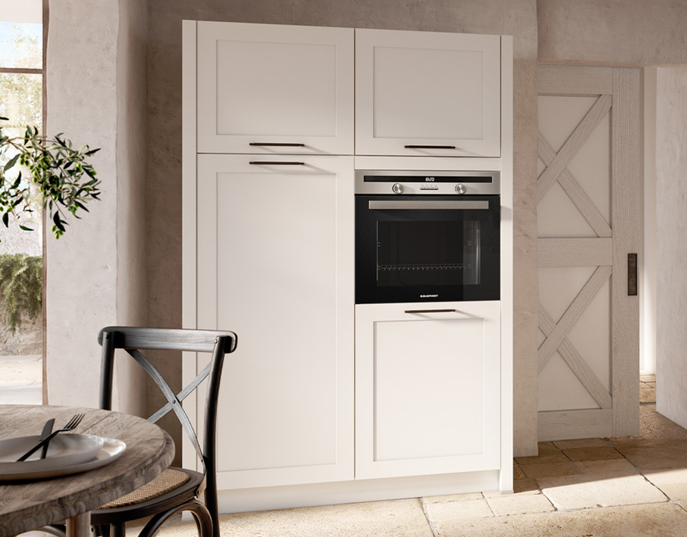 Weißer Einbauschrank im Landhausstil mit integriertem Backofen und schlichten Griffen, vor einer hellen Steinwand.